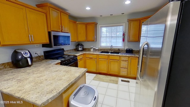 kitchen with appliances with stainless steel finishes, sink, light tile patterned floors, kitchen peninsula, and light stone countertops