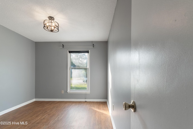 empty room featuring a textured ceiling, wood finished floors, and baseboards