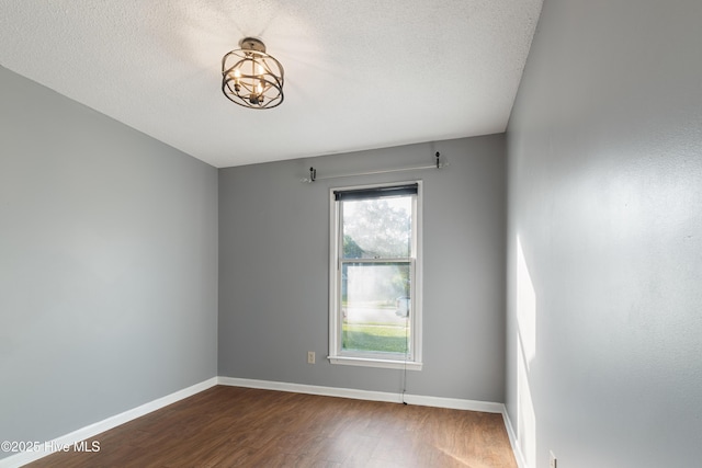 spare room featuring an inviting chandelier, a textured ceiling, baseboards, and dark wood-type flooring