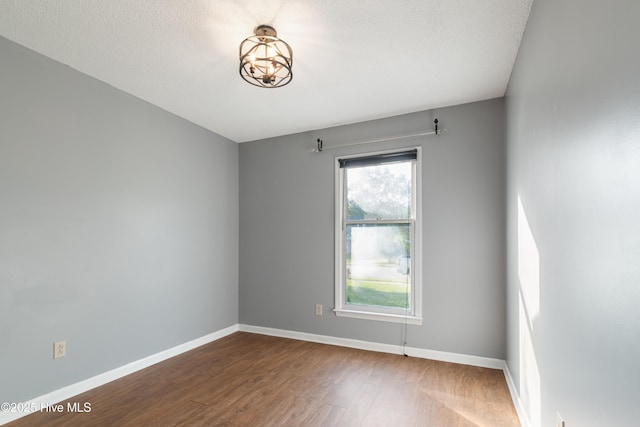 empty room featuring an inviting chandelier, a textured ceiling, wood finished floors, and baseboards