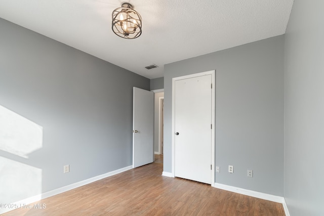 unfurnished bedroom featuring baseboards, a chandelier, visible vents, and wood finished floors