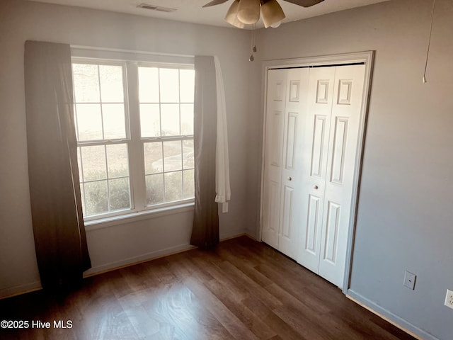 unfurnished bedroom featuring dark wood-type flooring, multiple windows, a closet, and visible vents