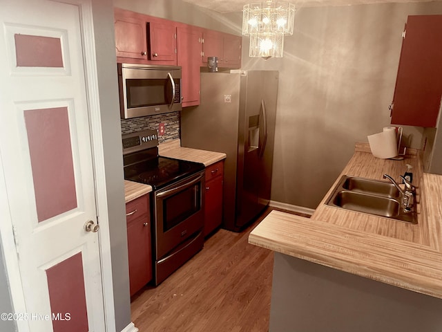 kitchen featuring light wood-style flooring, a sink, light countertops, appliances with stainless steel finishes, and decorative light fixtures