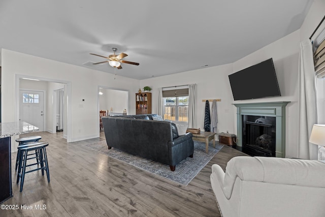 living room with ceiling fan, a high end fireplace, and light hardwood / wood-style flooring