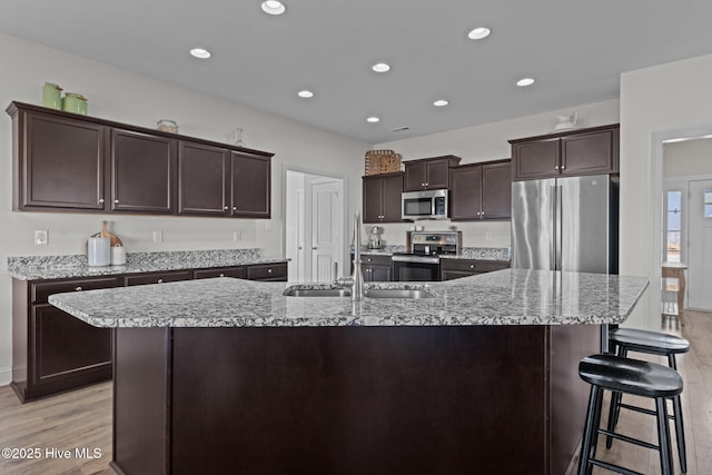 kitchen with appliances with stainless steel finishes, dark brown cabinets, a center island with sink, and light wood-type flooring