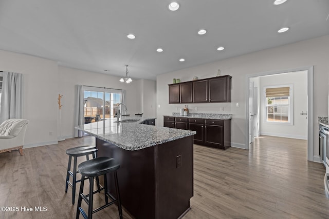 kitchen with dark brown cabinetry, sink, hanging light fixtures, a center island with sink, and light hardwood / wood-style flooring