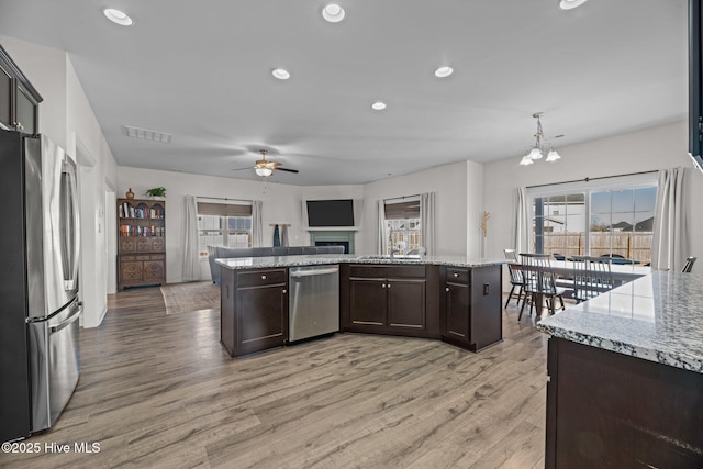 kitchen with pendant lighting, dark brown cabinetry, appliances with stainless steel finishes, and light stone counters