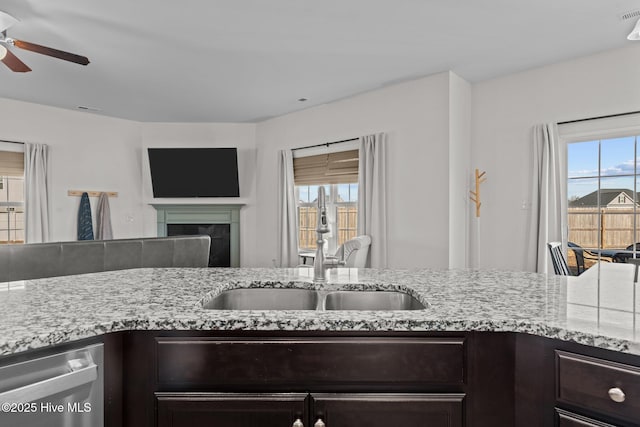 kitchen with sink, light stone counters, dark brown cabinets, dishwasher, and ceiling fan