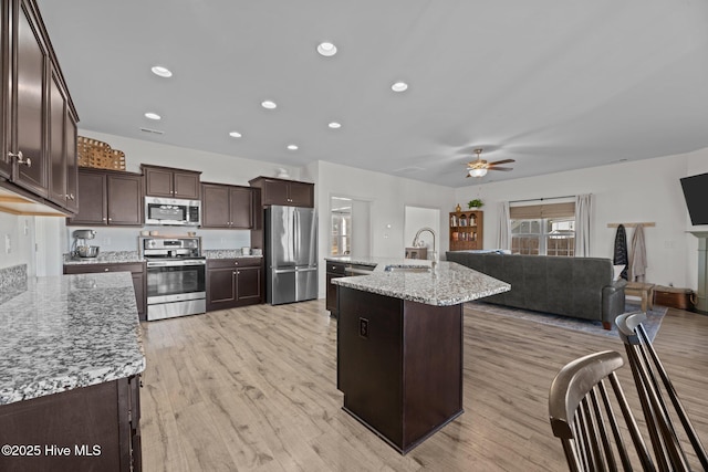 kitchen featuring sink, light wood-type flooring, an island with sink, stainless steel appliances, and light stone countertops