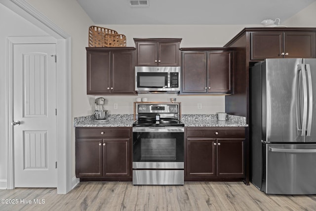 kitchen featuring dark brown cabinetry, light wood-type flooring, light stone countertops, and appliances with stainless steel finishes