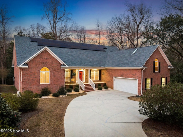 view of front of house with solar panels, brick siding, roof with shingles, and concrete driveway