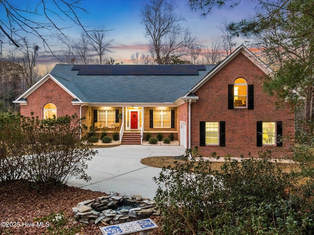 view of front of property featuring brick siding, solar panels, driveway, and a shingled roof