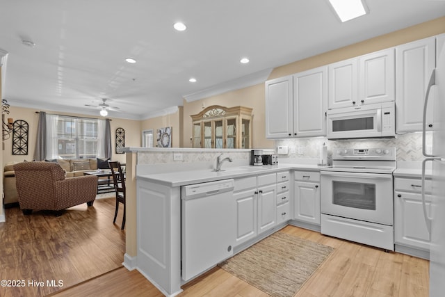 kitchen with light hardwood / wood-style floors, white cabinets, white appliances, and kitchen peninsula