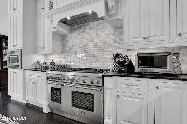 kitchen featuring white cabinetry, dark countertops, stainless steel appliances, and premium range hood