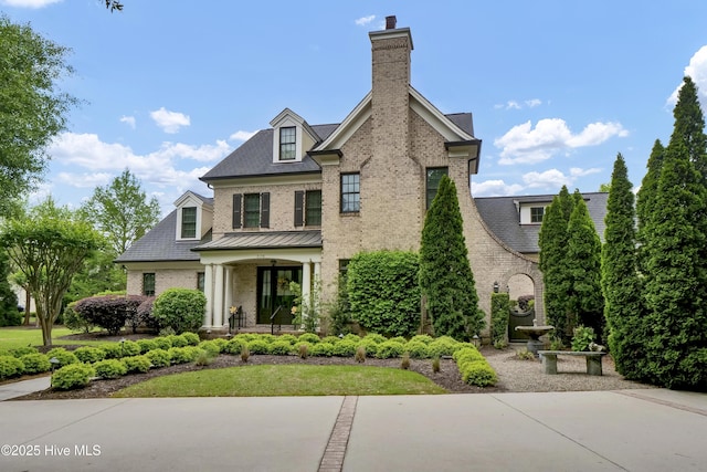 view of front of home featuring a chimney, a porch, and brick siding