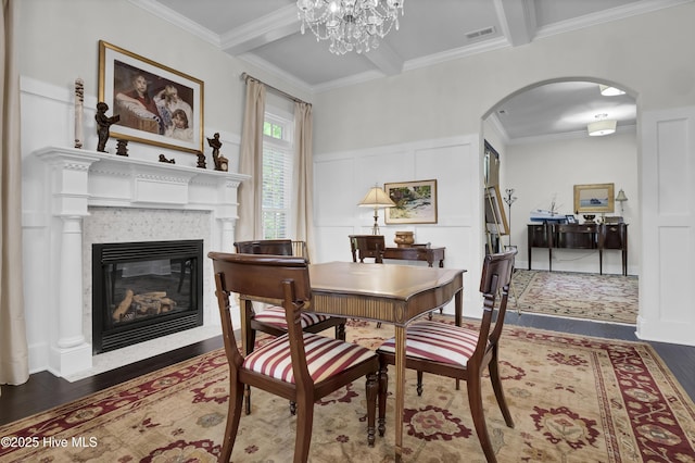 dining space featuring a glass covered fireplace, visible vents, wood finished floors, arched walkways, and beamed ceiling
