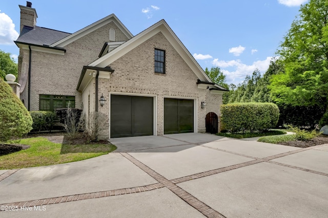 view of side of home featuring brick siding, driveway, a chimney, and a garage