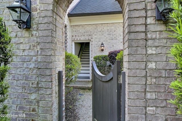 doorway to property with roof with shingles and brick siding