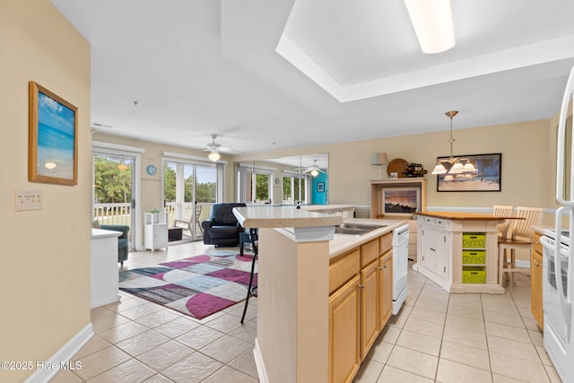 kitchen featuring light brown cabinetry, light tile patterned floors, pendant lighting, white appliances, and a kitchen island with sink