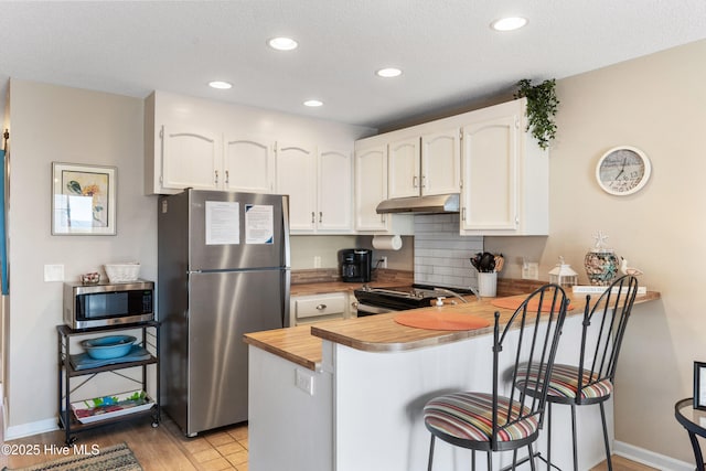 1505 Carolina Beach Ave N Unit 2F, Carolina Beach, NC 28428 - kitchen featuring stainless steel appliances, under cabinet range hood, a peninsula, white cabinets, and a breakfast bar
