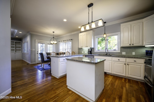 kitchen featuring a kitchen island, white cabinets, dark stone counters, hanging light fixtures, and ornamental molding