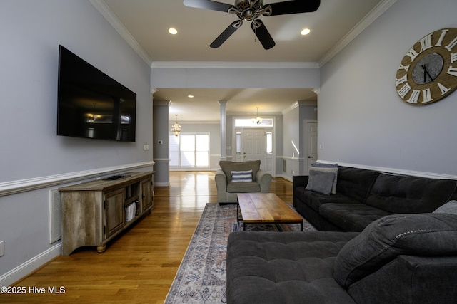 living room featuring crown molding, ceiling fan with notable chandelier, decorative columns, and light wood-type flooring