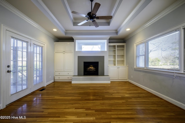 unfurnished living room with dark wood-type flooring, ornamental molding, a tray ceiling, ceiling fan, and a tiled fireplace