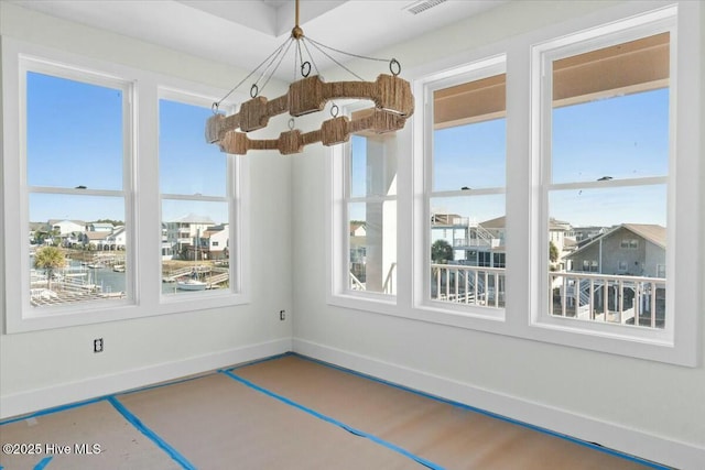 unfurnished dining area featuring a chandelier, a healthy amount of sunlight, and baseboards