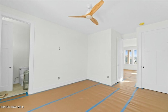 unfurnished bedroom with baseboards, ensuite bath, wood finished floors, and a ceiling fan