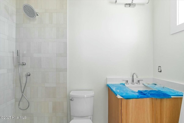 bathroom with toilet, tiled shower, and vanity