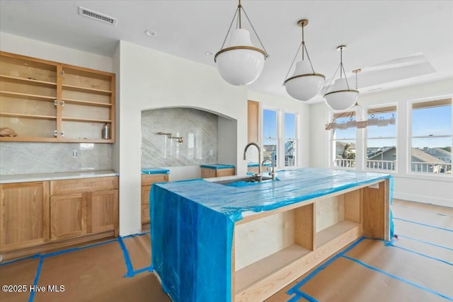 kitchen featuring visible vents, an island with sink, a sink, open shelves, and light countertops