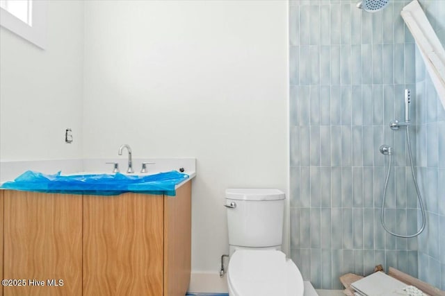 full bathroom with a tile shower, toilet, and vanity