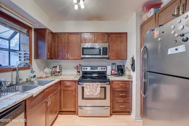 kitchen with appliances with stainless steel finishes, sink, light wood-type flooring, light stone countertops, and a textured ceiling