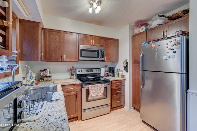 kitchen featuring sink, a textured ceiling, light wood-type flooring, stainless steel appliances, and light stone countertops