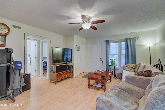 living room featuring ceiling fan, a textured ceiling, and light wood-type flooring