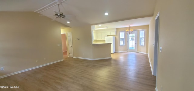 unfurnished living room with ceiling fan with notable chandelier, light hardwood / wood-style floors, and vaulted ceiling with beams