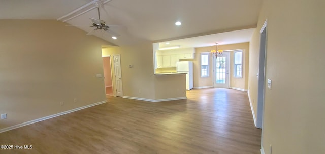 unfurnished living room featuring ceiling fan with notable chandelier, light hardwood / wood-style floors, and lofted ceiling with beams