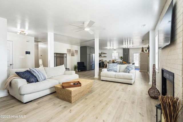 living room with ceiling fan, a fireplace, and light wood-type flooring