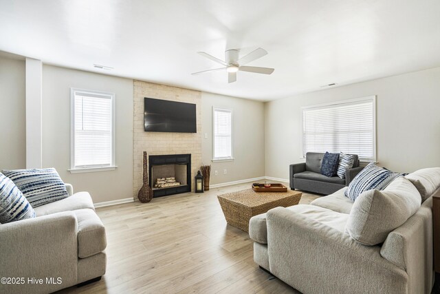 living room featuring ceiling fan, a fireplace, and light hardwood / wood-style floors