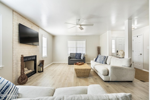 living room featuring a brick fireplace, a ceiling fan, baseboards, and wood finished floors