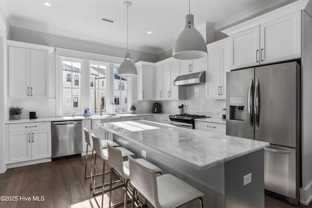 kitchen featuring dark wood-style flooring, white cabinets, under cabinet range hood, appliances with stainless steel finishes, and crown molding