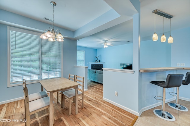 dining space with ceiling fan with notable chandelier and light wood-type flooring