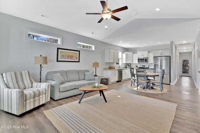 living room with ceiling fan, lofted ceiling, and light hardwood / wood-style flooring