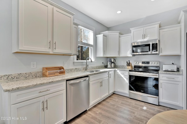 kitchen featuring sink, white cabinetry, light wood-type flooring, stainless steel appliances, and light stone countertops