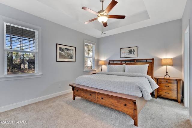 carpeted bedroom with ceiling fan and a tray ceiling