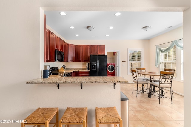 kitchen featuring a breakfast bar, light tile patterned floors, kitchen peninsula, washer / clothes dryer, and black appliances