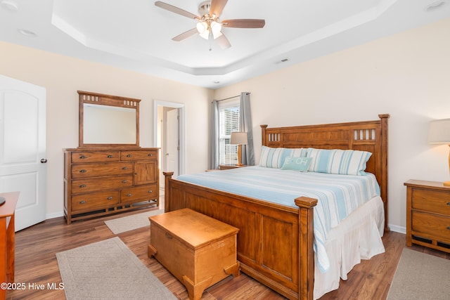 bedroom with ceiling fan, wood-type flooring, and a raised ceiling