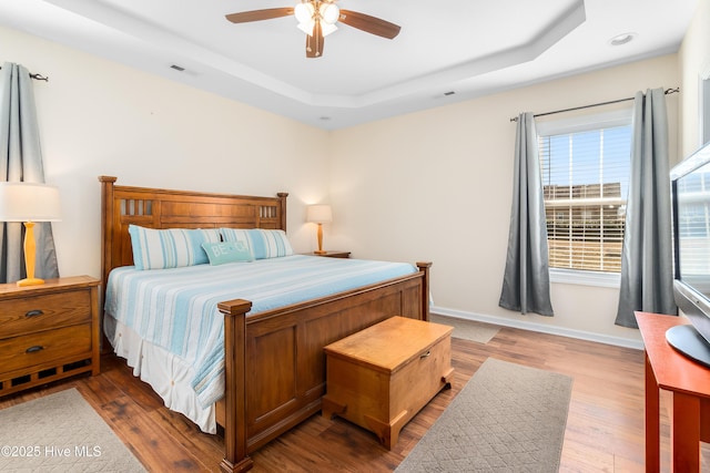 bedroom with a raised ceiling, hardwood / wood-style floors, and ceiling fan