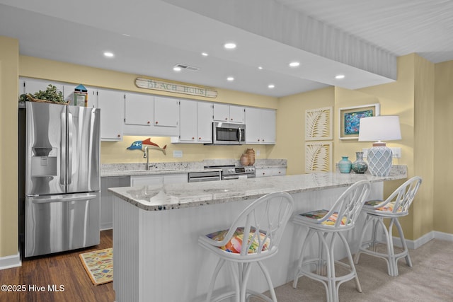 kitchen with white cabinetry, a breakfast bar, appliances with stainless steel finishes, and light stone countertops