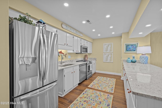 kitchen with sink, white cabinetry, light stone counters, appliances with stainless steel finishes, and hardwood / wood-style floors